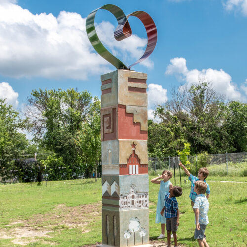 Photograph of the St. John Community Pillar sculpture with children pointing at it in a park.