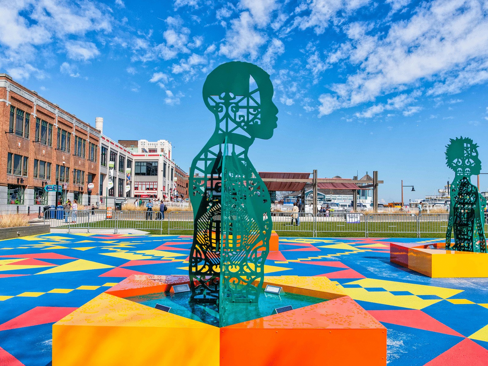 A green sculpture of a man placed on top of a very colorful cement block.