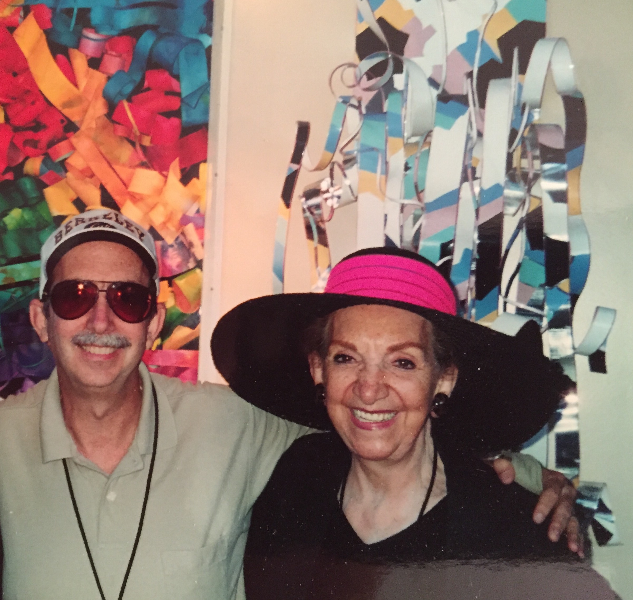 An image of Dorothy Gillespie and her son Gary standing in front of her artwork hugging one another.