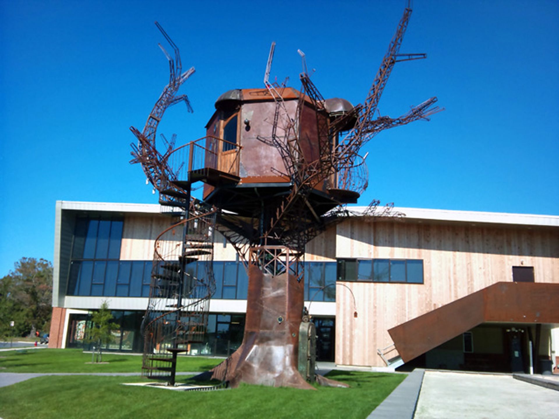 A large brown tree house sculpture placed outside in front of a building.