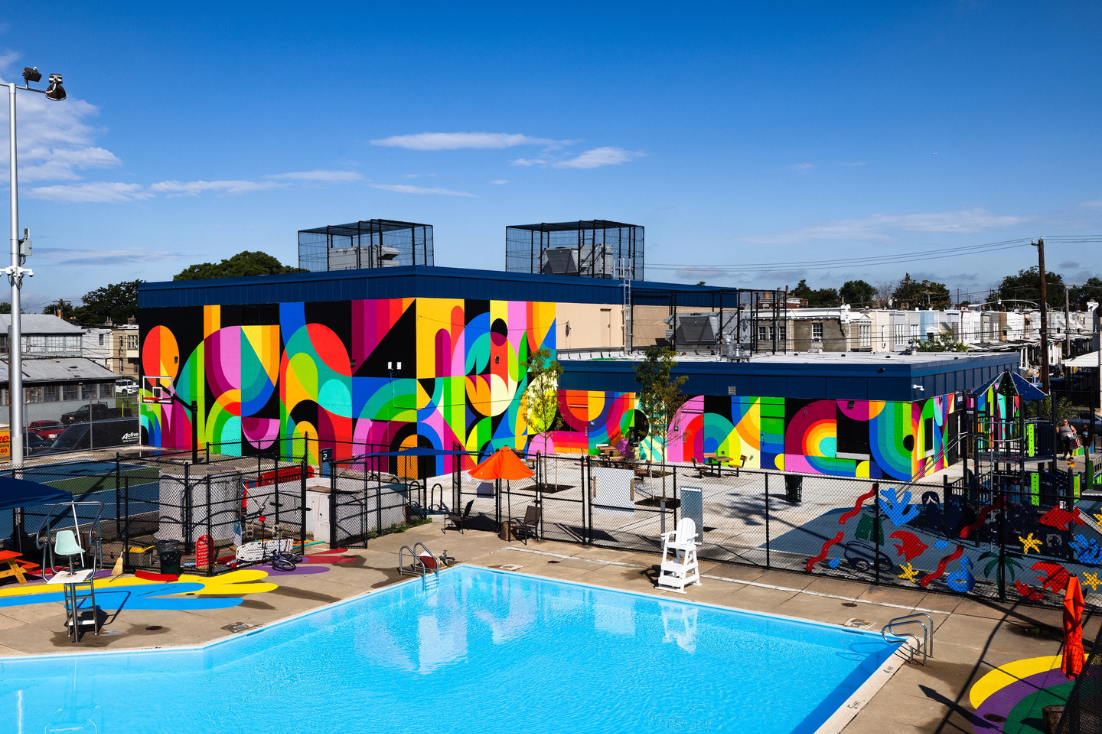 Colorful abstract mural painted on a building outside by a pool with colorful random shapes on the floor.