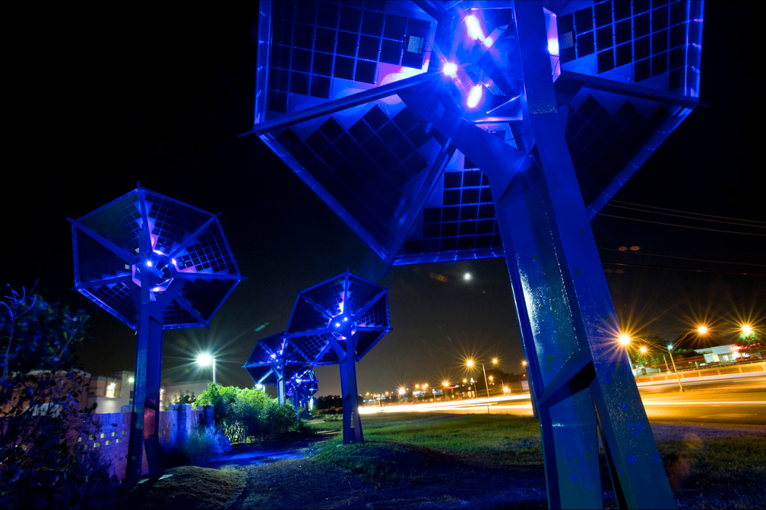 Several florescent blue light posts are placed outside by a highway.