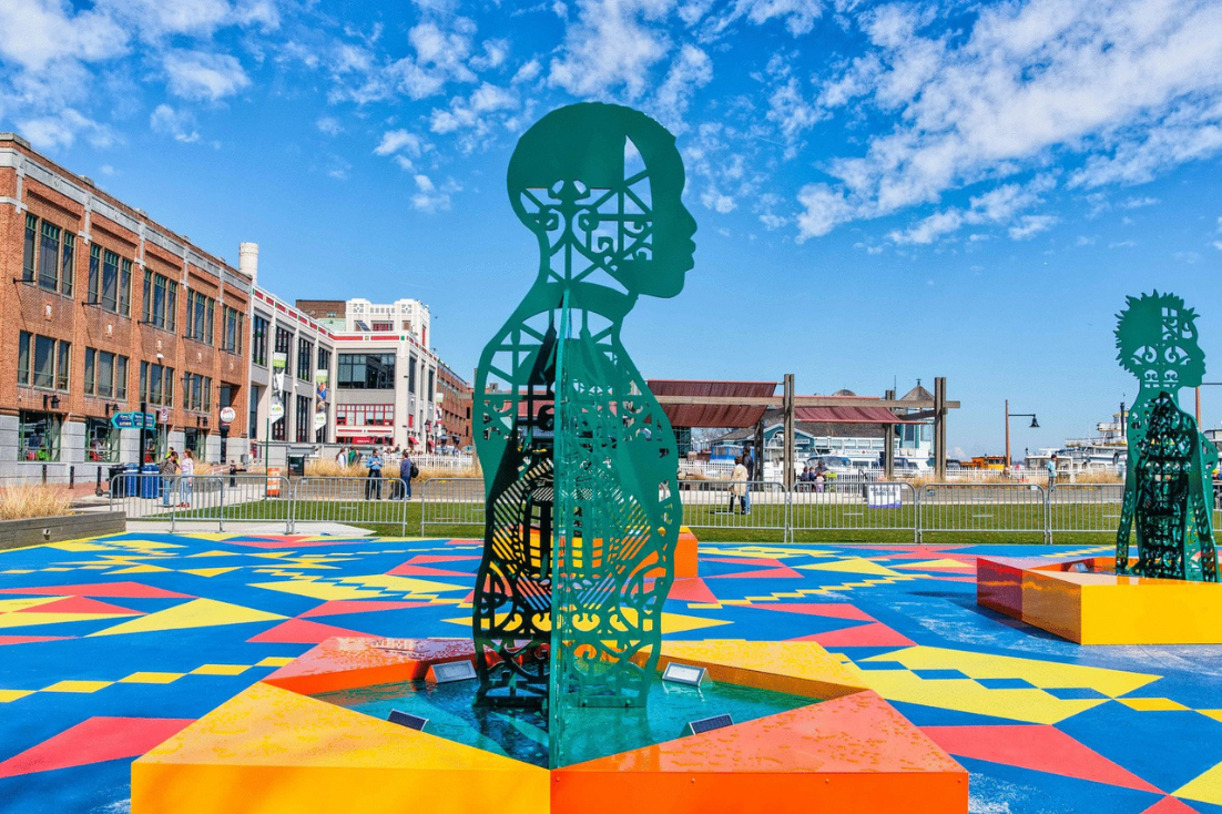 A large dark green sculpture of a man's upper body is placed outside on top of a colorful block.