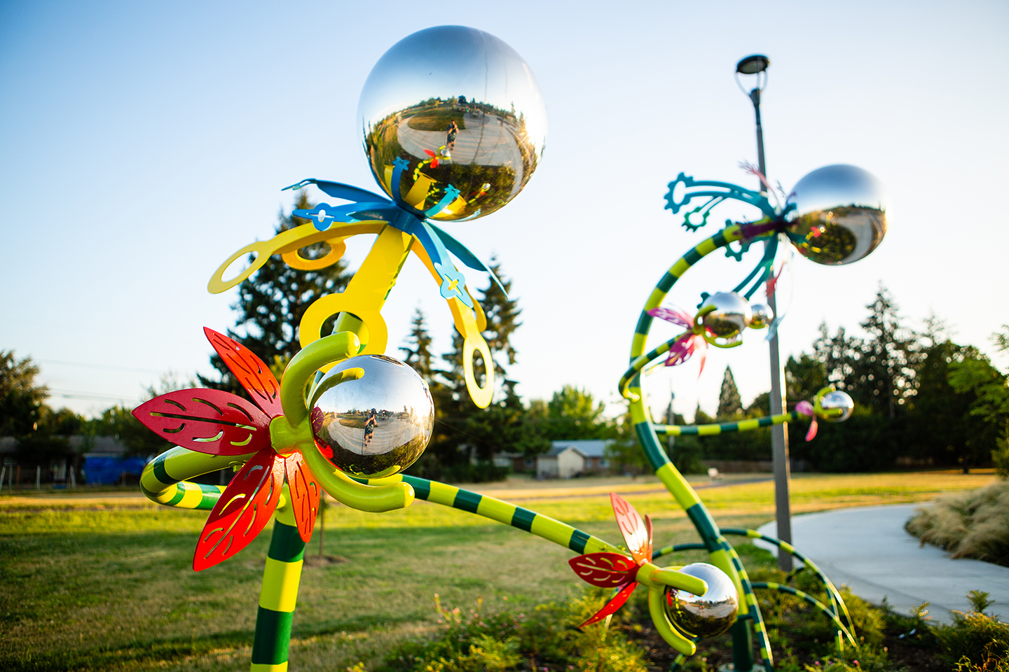 Colorful metal sculptures with reflective silver spheres are displayed in an outdoor setting.