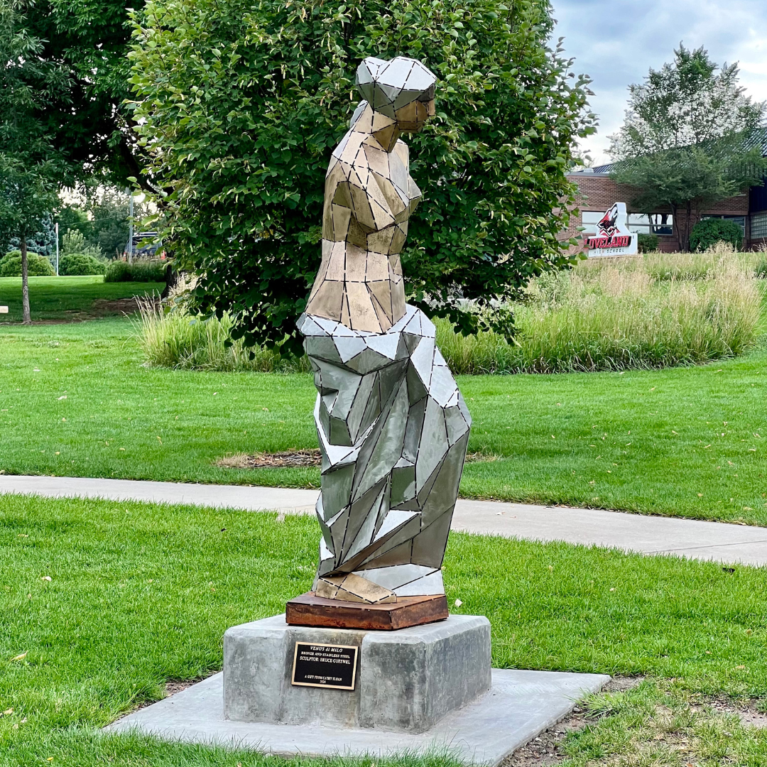 A large gold and silver sculpture of a woman placed outside in front of a building.