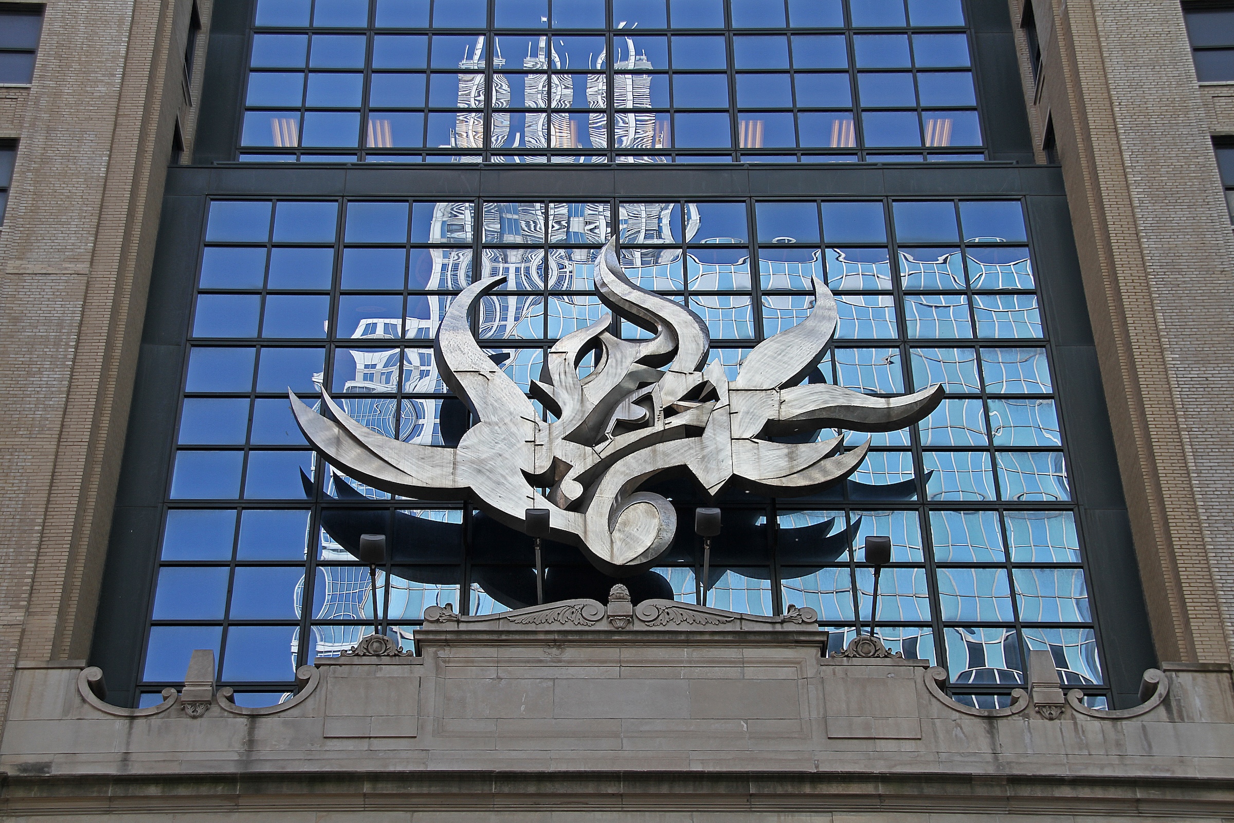 A building facade with reflective glass windows and an abstract metallic sculpture.